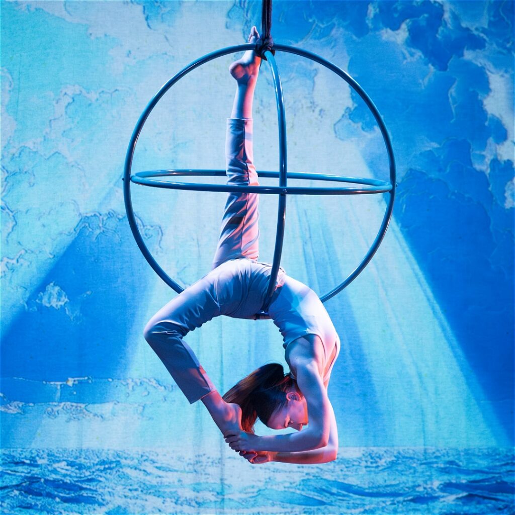 Circus Scorpius an performer hangs from a metal orb